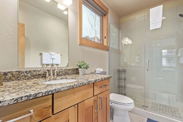 A bathroom with a granite countertop, a sink, a mirror, a toilet, and a glass-enclosed shower.