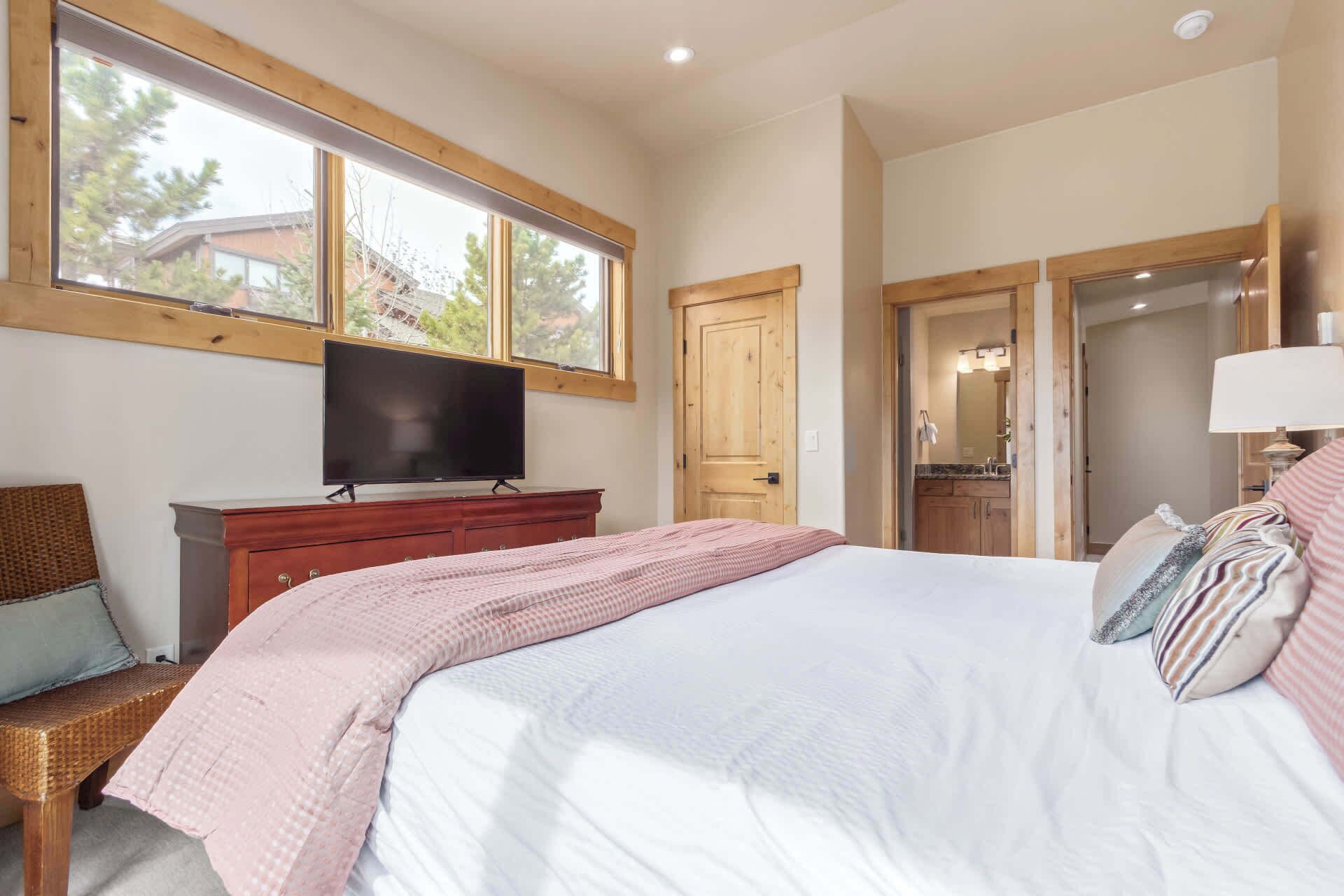 A bedroom with a large bed, a television on a wooden dresser, a window, and a door leading to a bathroom.
