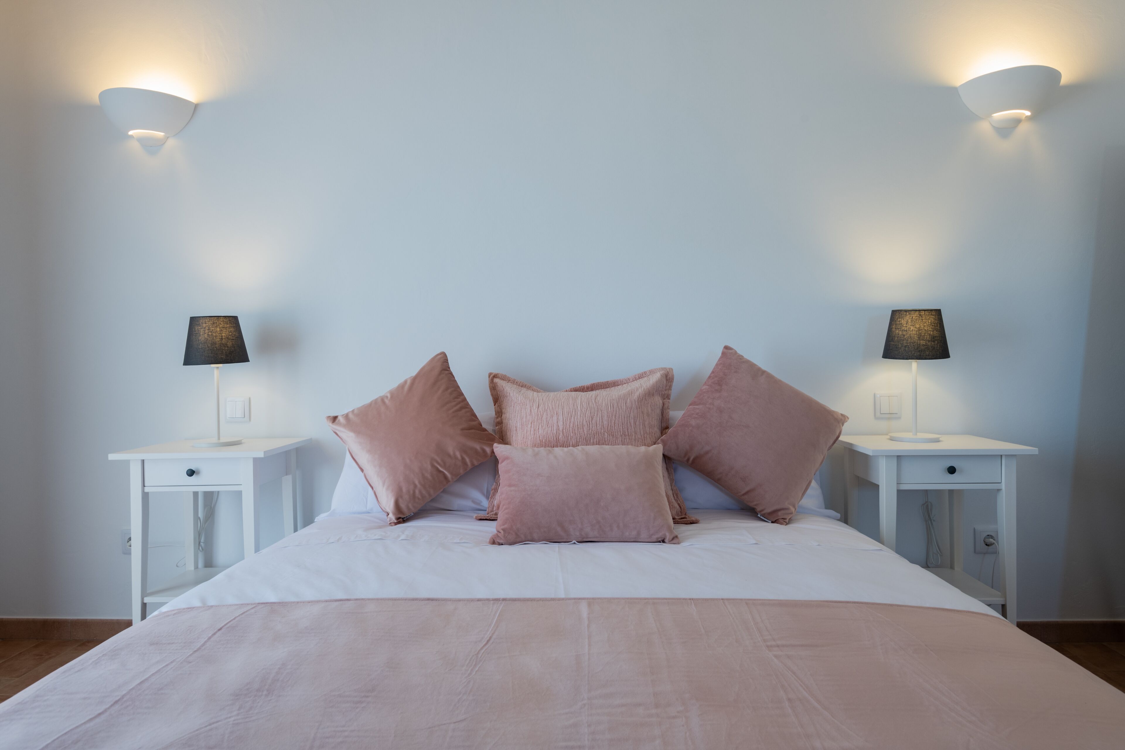 A bedroom with a bed, two bedside tables, and wall-mounted lamps.