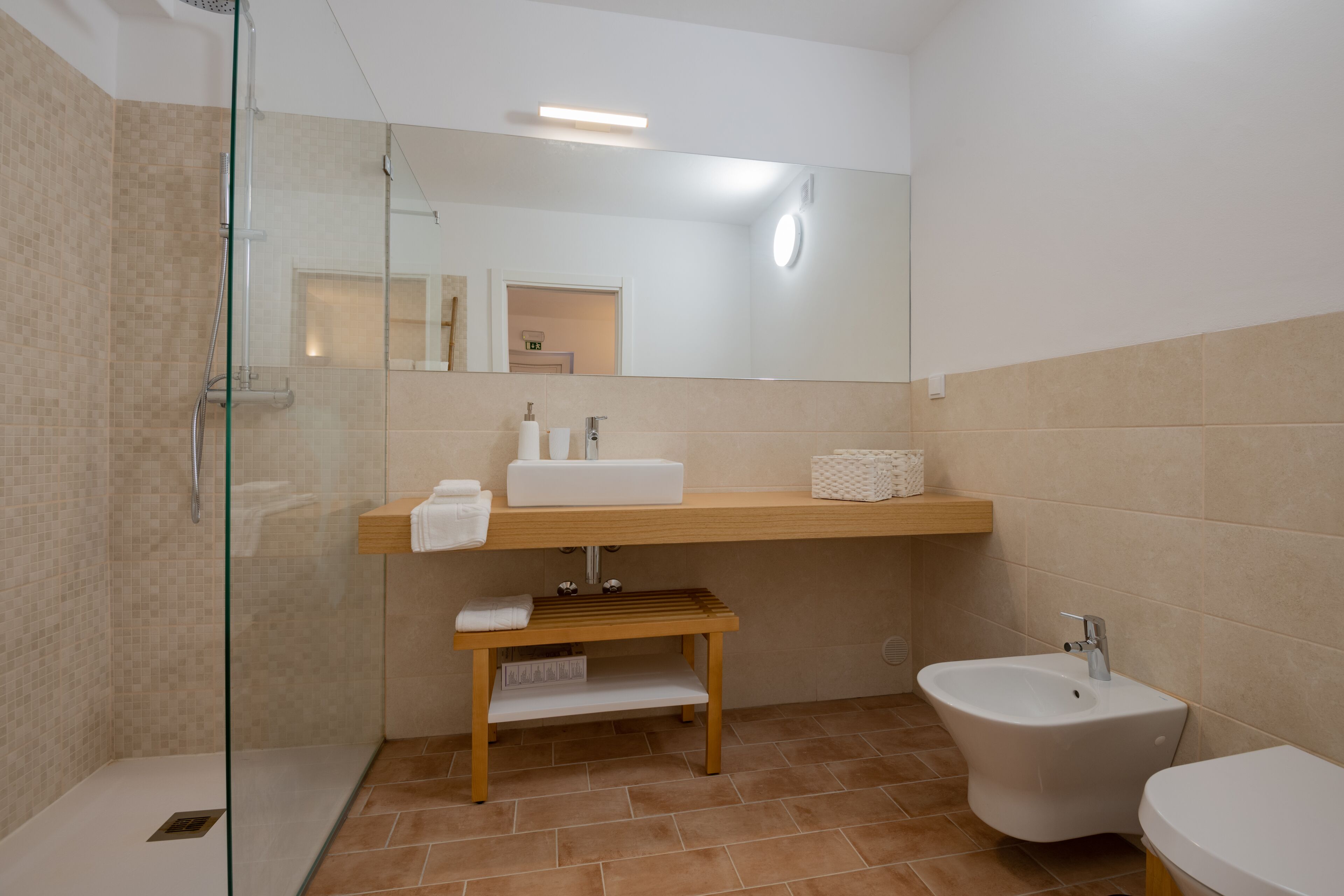 Un baño moderno con cabina de ducha de vidrio, tocador de madera con lavamanos, un bidé y un espejo.