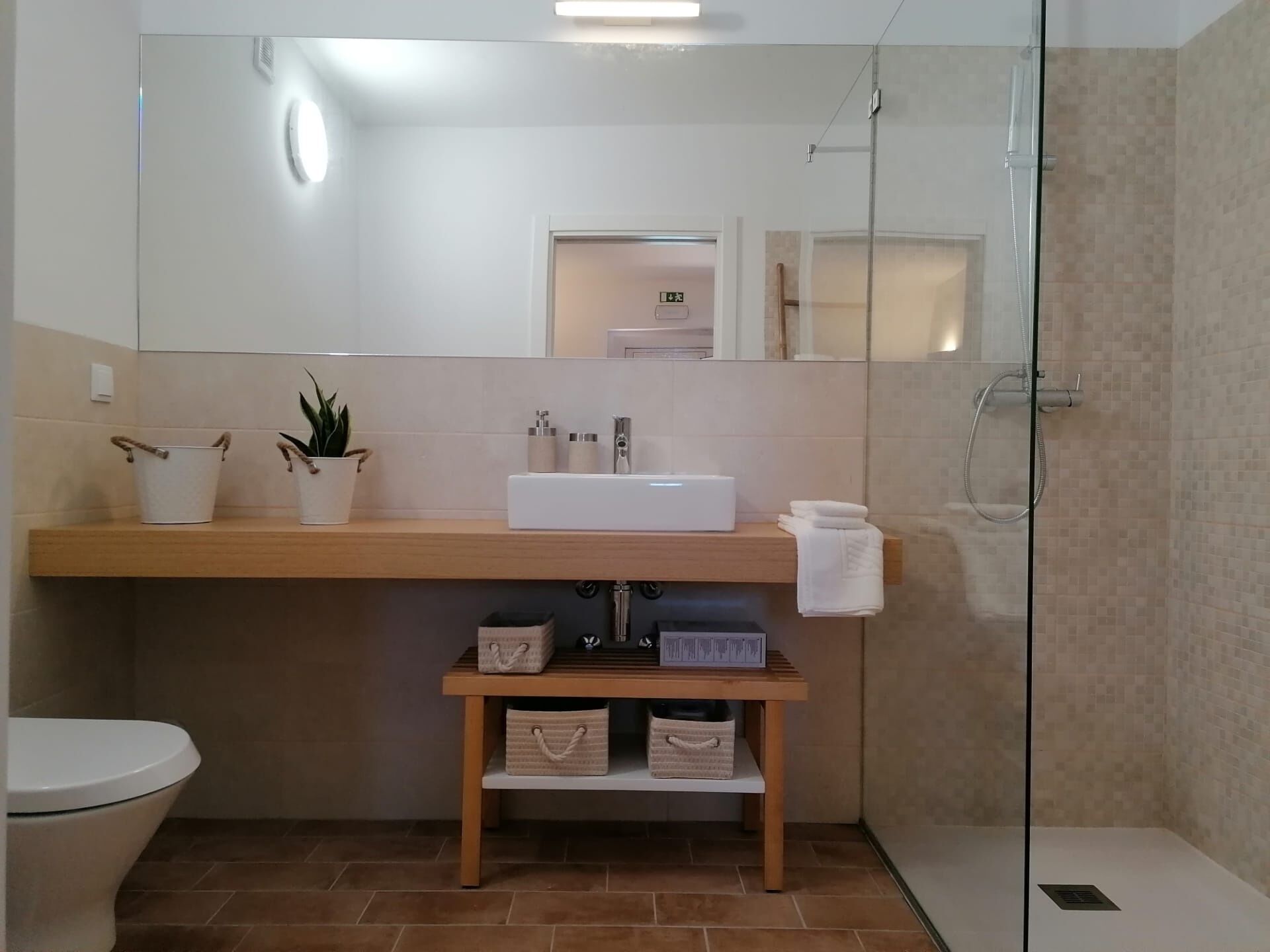 A modern bathroom with a wooden vanity, a white sink, a mirror, a glass shower enclosure, and a toilet.