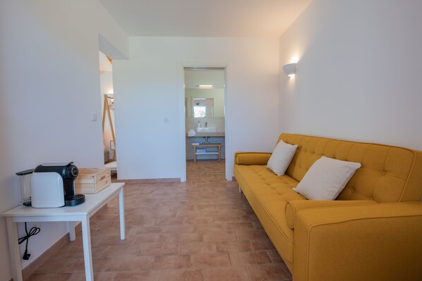 A modern living room with a yellow sofa, a white coffee table, and a kitchen area in the background.