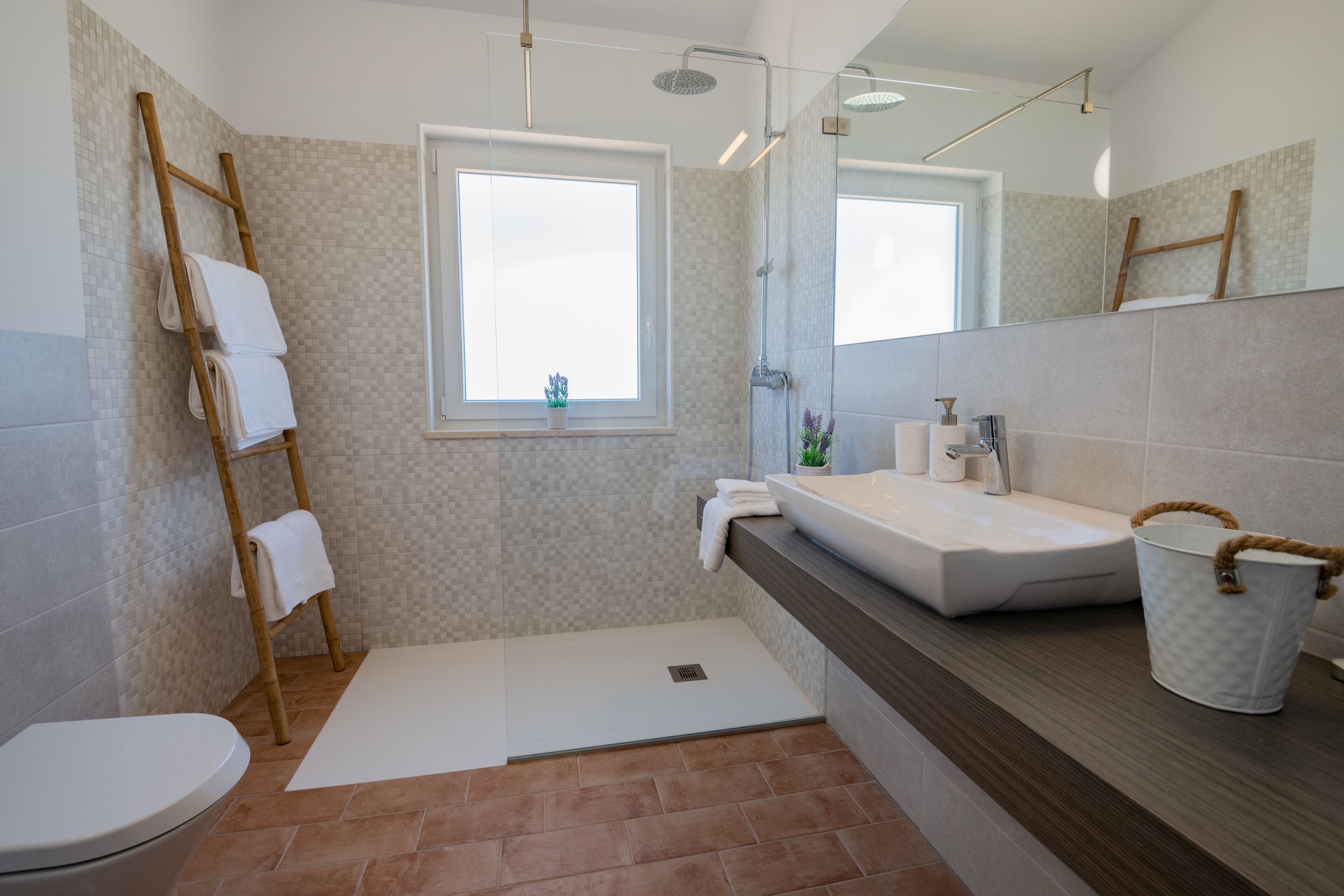 Une salle de bain moderne dotée d’une grande fenêtre, d’une douche, de toilettes et d’un lavabo.