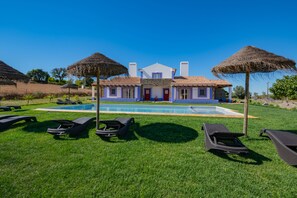 A poolside area with lounge chairs and a house in the background.