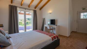 A bedroom with a bed, a desk, a chair, a TV, and a sliding glass door leading to a balcony.