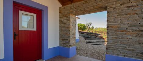 A red door with a window, a stone wall, and a view of a garden.