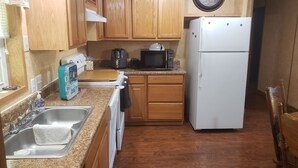 A compact kitchen with wooden cabinets, a white refrigerator, a microwave, a coffee maker, and a sink with a towel.