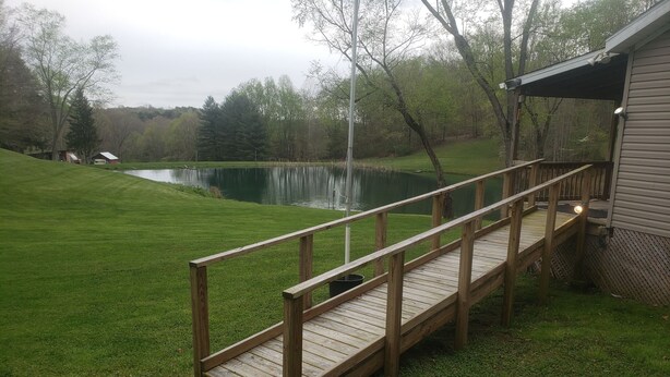 A wooden deck leading to a house with a pond in the background.