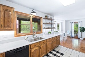 A kitchen with wooden cabinets, a dishwasher, a sink, and a window with a view of greenery.
