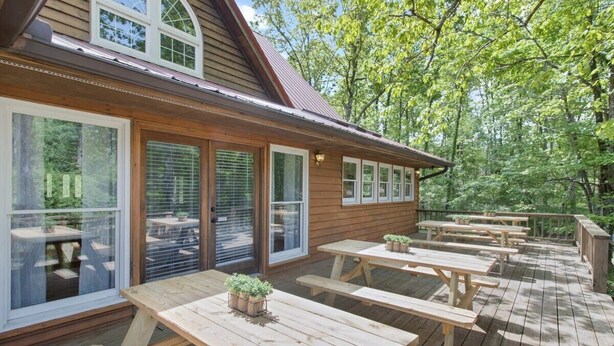Une terrasse en bois avec des tables de pique-nique et un bâtiment doté de grandes fenêtres.