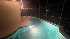 Une piscine intérieure dont les bords sont recouverts de carreaux, entourée d’un espace abrité comprenant des chaises et des guirlandes lumineuses.