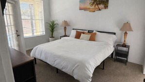 Une chambre à coucher comprenant un lit, un ventilateur de plafond, une fenêtre avec des stores et un tableau accroché au mur.