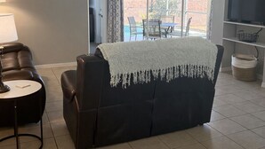 Un salon comprenant un canapé, une table, un ventilateur de plafond et donnant sur une terrasse extérieure.