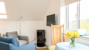 A cozy living room with a blue sofa, a wooden chair, a small table with a blue tablecloth, and a vase of yellow flowers. - Gerry's Place (Church Stretton)