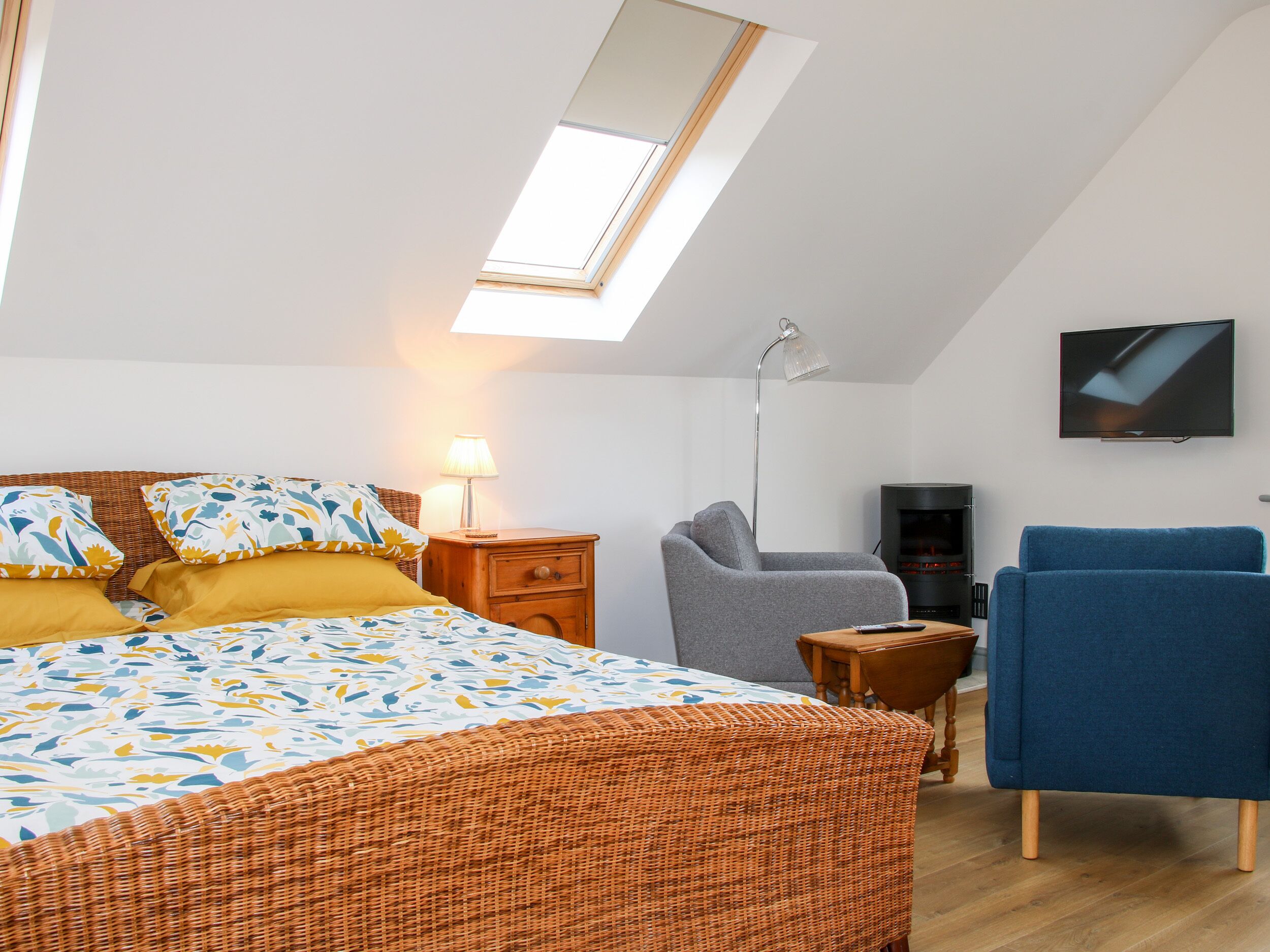 A bedroom with a bed, a desk, a chair, a TV, and a skylight.