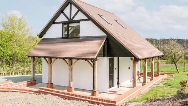 A modern two-story house with a sloped roof, a covered porch, and a brick foundation. - Gerry's Place (Church Stretton)