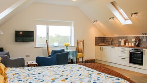 A modern loft bedroom with a large bed, a dining area, and a kitchenette. - Gerry's Place (Church Stretton)