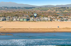 A coastal residential area with houses along the beach, a clear sky, and distant hills.