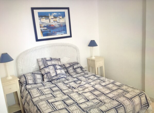 A neatly made bed with a patterned bedspread and pillows, two bedside tables with lamps, and a framed painting on the wall.