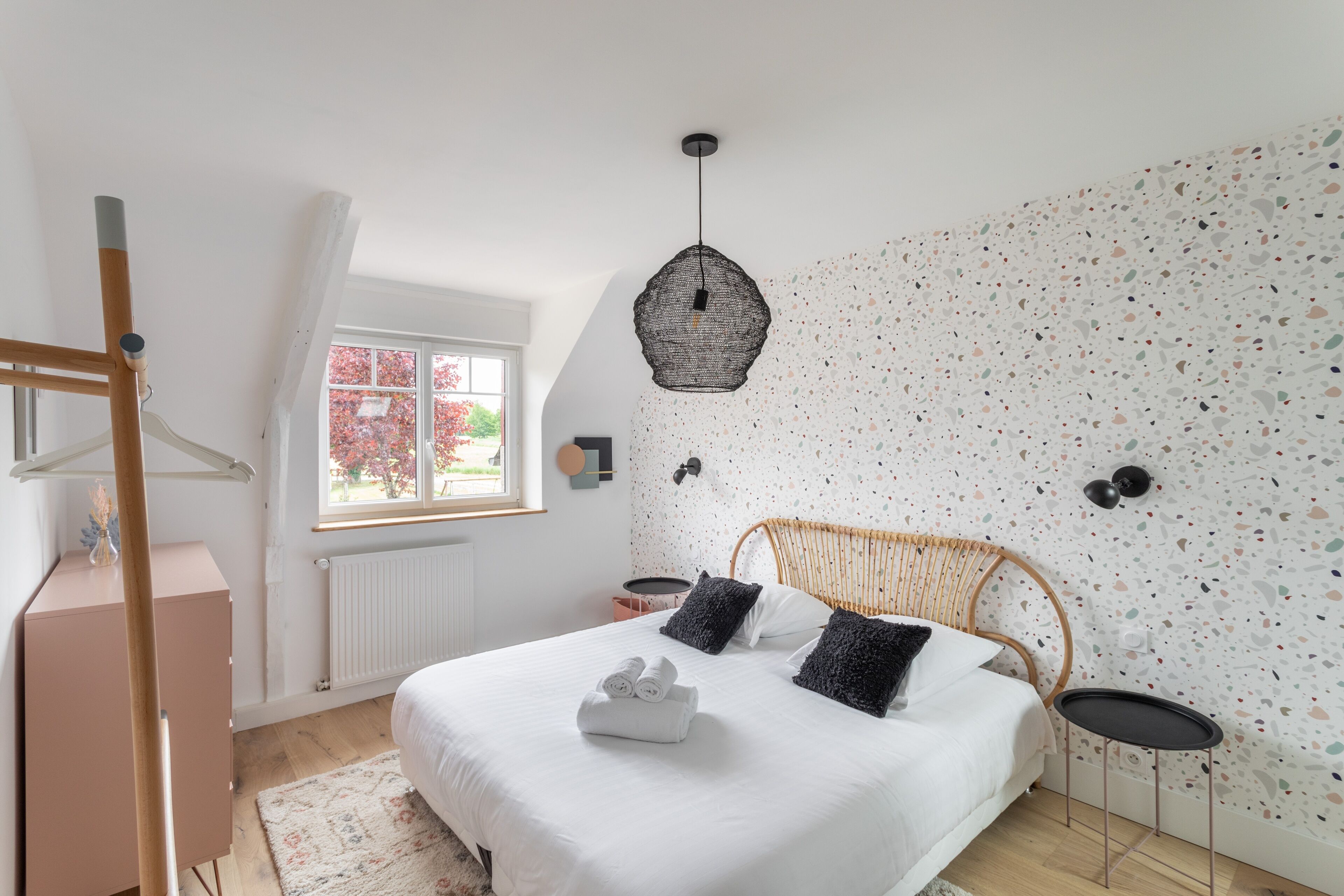 Un dormitorio con cama, lámpara colgante, ventana y pared con diseño moteado.
