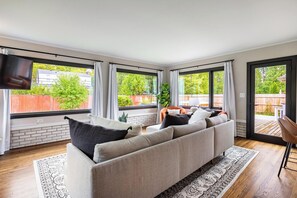 A modern living room with a large sofa, a flat-screen TV, and large windows with curtains.