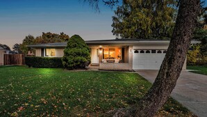 A two-story house with a garage, a well-maintained lawn, and a large tree in the foreground. - Spacious, Elegant Home w/ Cozy Backyard! (Troy)