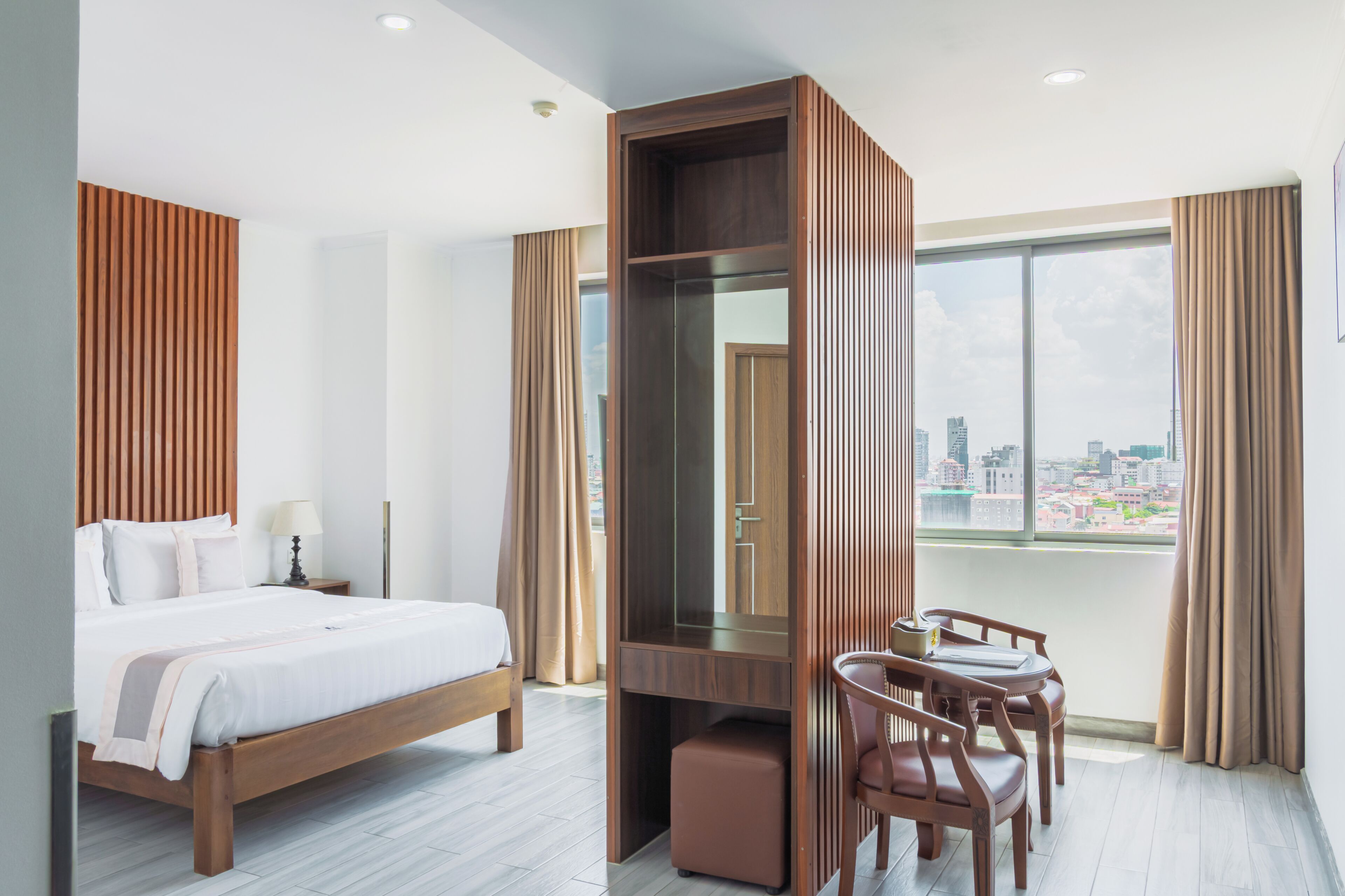 Habitación de hotel con cama, escritorio, silla, espejo y una ventana grande con vistas a la ciudad.