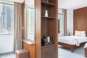 Une chambre d’hôtel avec une grande fenêtre, un lit, une armoire en bois et une petite table avec une bouilloire.