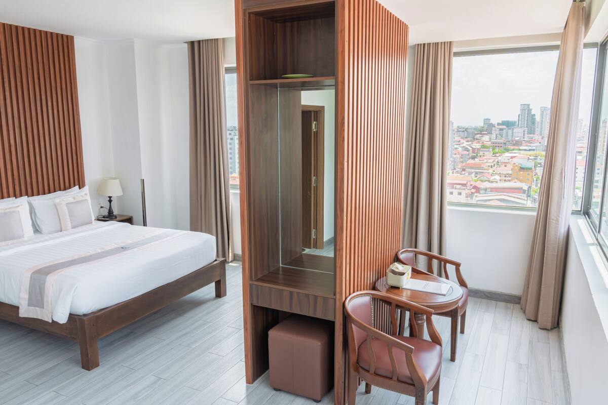 A hotel room with a bed, a desk, a chair, a mirror, and a city view.