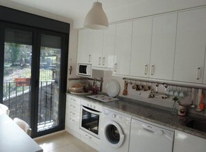 A modern kitchen with white cabinets, a built-in oven, a washing machine, and a microwave.