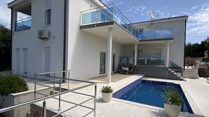 A modern two-story house with a swimming pool, outdoor seating, and a glass balustrade.