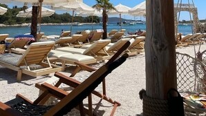 A beachside lounge area with wooden lounge chairs, white umbrellas, and a wooden post with rope decorations.
