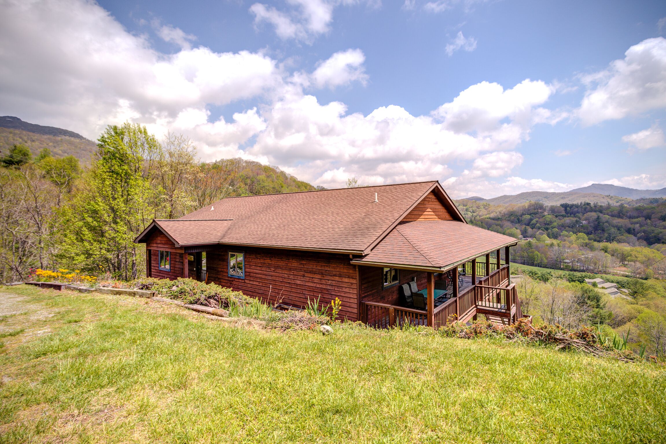 Eine Holzhütte mit Veranda, umgeben von einer grünen Landschaft und Bergen im Hintergrund.
