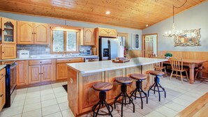 Una cocina amplia con armarios de madera, una isla grande con taburetes, un refrigerador y un comedor con sillas.