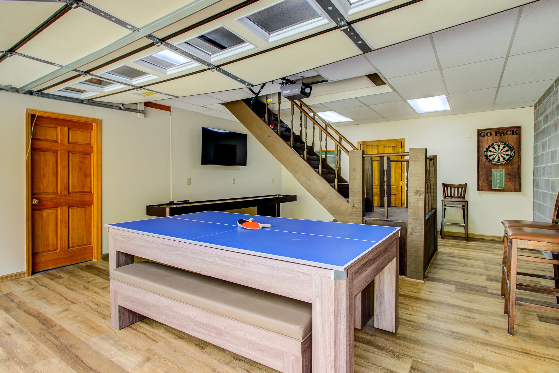 A room with a ping pong table, a staircase, a dartboard, and a wooden door.