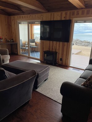 Ein gemütliches Wohnzimmer mit einem großen Flachbildfernseher, bequemen Sitzgelegenheiten und Blick auf den Strand durch große Schiebetüren.