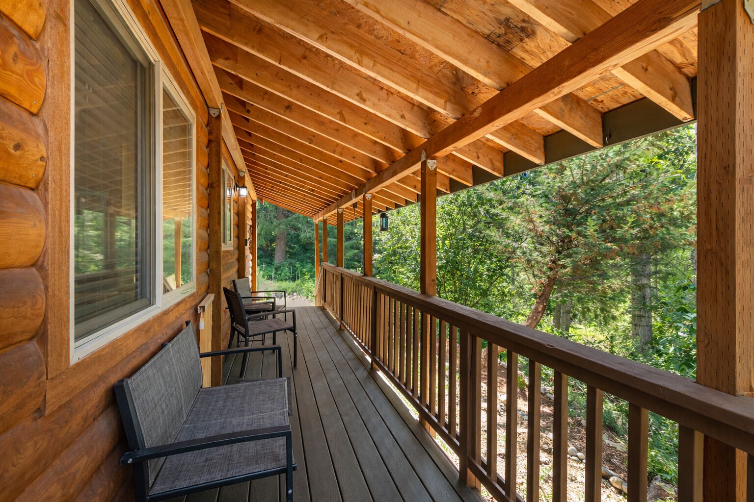 Eine Holzterrasse mit Geländer, zwei Stühlen und Blick auf einen Wald.