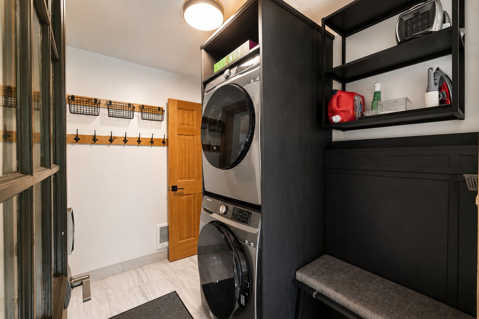 Une buanderie équipée d’un lave-linge et d’un sèche-linge à chargement frontal, d’une porte en bois et d’un banc.