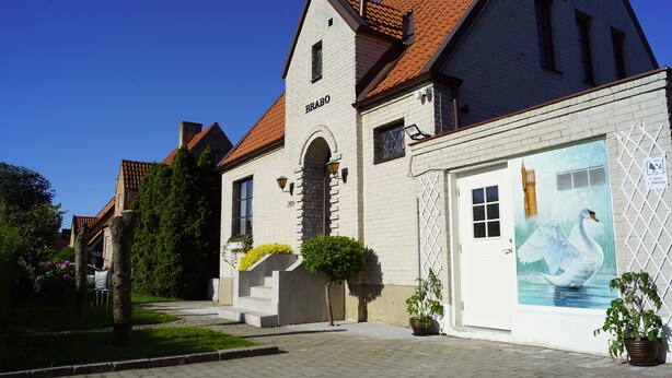 A building with a white facade, a red-tiled roof, and a mural of a swan on the right side.