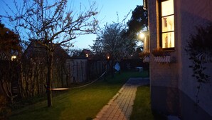 A pathway leading to a building with a window. There are trees and a fence in the background.