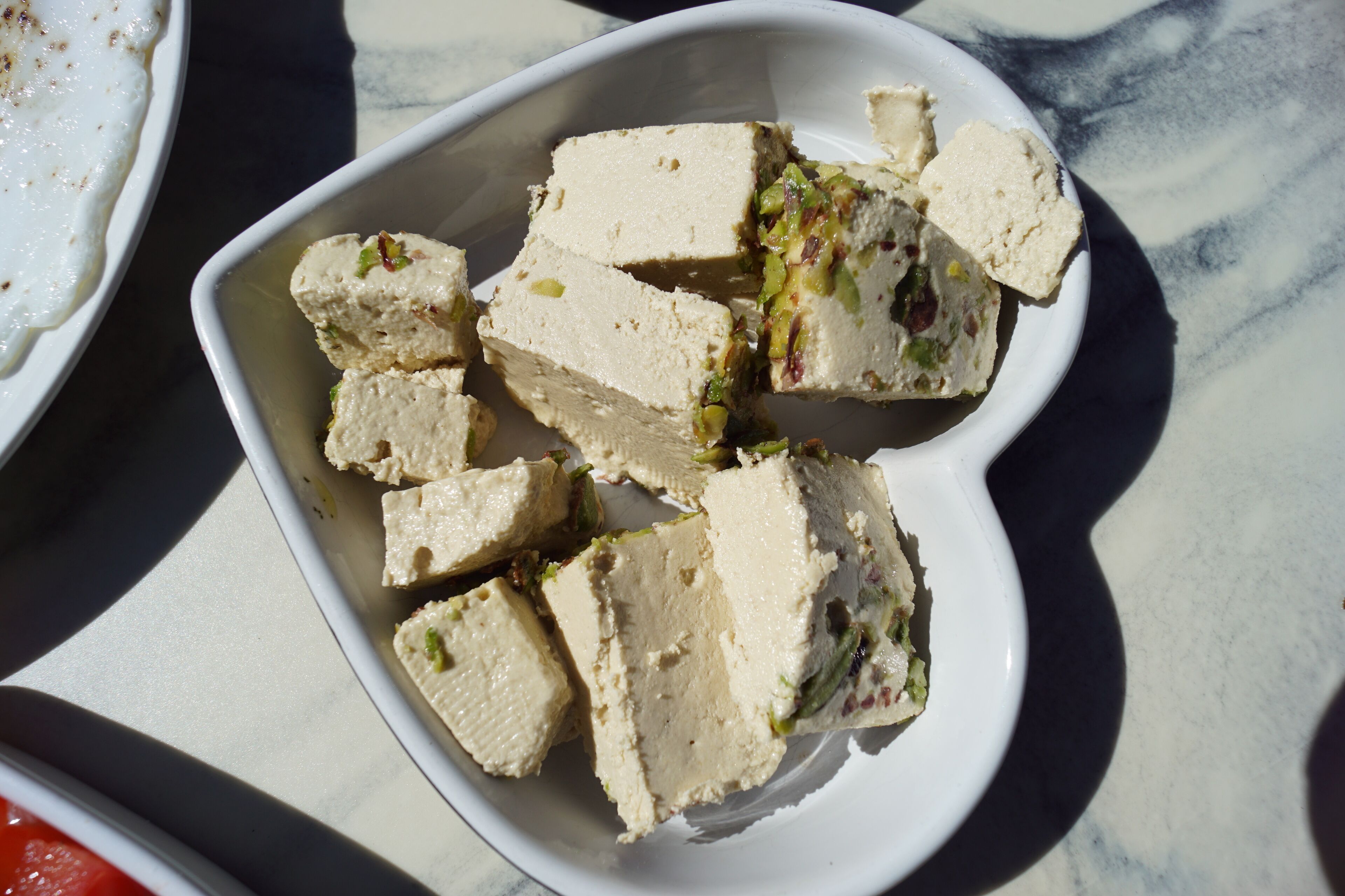 Een witte schaal met blokjes eten, mogelijk tofu, versierd met groene kruiden, op een marmeren oppervlak.