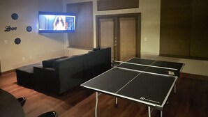 A room with a TV mounted on the wall, a sofa, and two ping pong tables. - Entire Apt • 1br w/private balcony SouthWest Houston (Houston)