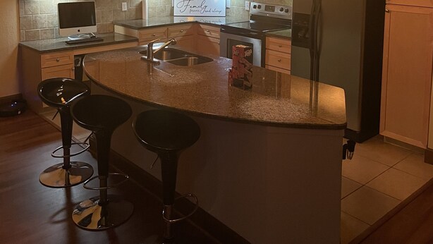 A modern kitchen with wooden cabinets, a central island with bar stools, a refrigerator, a microwave, and a sign that reads "Family". - Entire Apt • 1br w/private balcony SouthWest Houston (Houston)