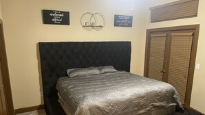 A bedroom with a large bed, a dark headboard, and a door with a window. There are two wall decorations and a light fixture above the bed. - Entire Apt • 1br w/private balcony SouthWest Houston (Houston)