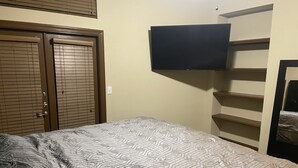 A bedroom with a bed, a wardrobe, a television mounted on the wall, and a shelf unit. - Entire Apt • 1br w/private balcony SouthWest Houston (Houston)