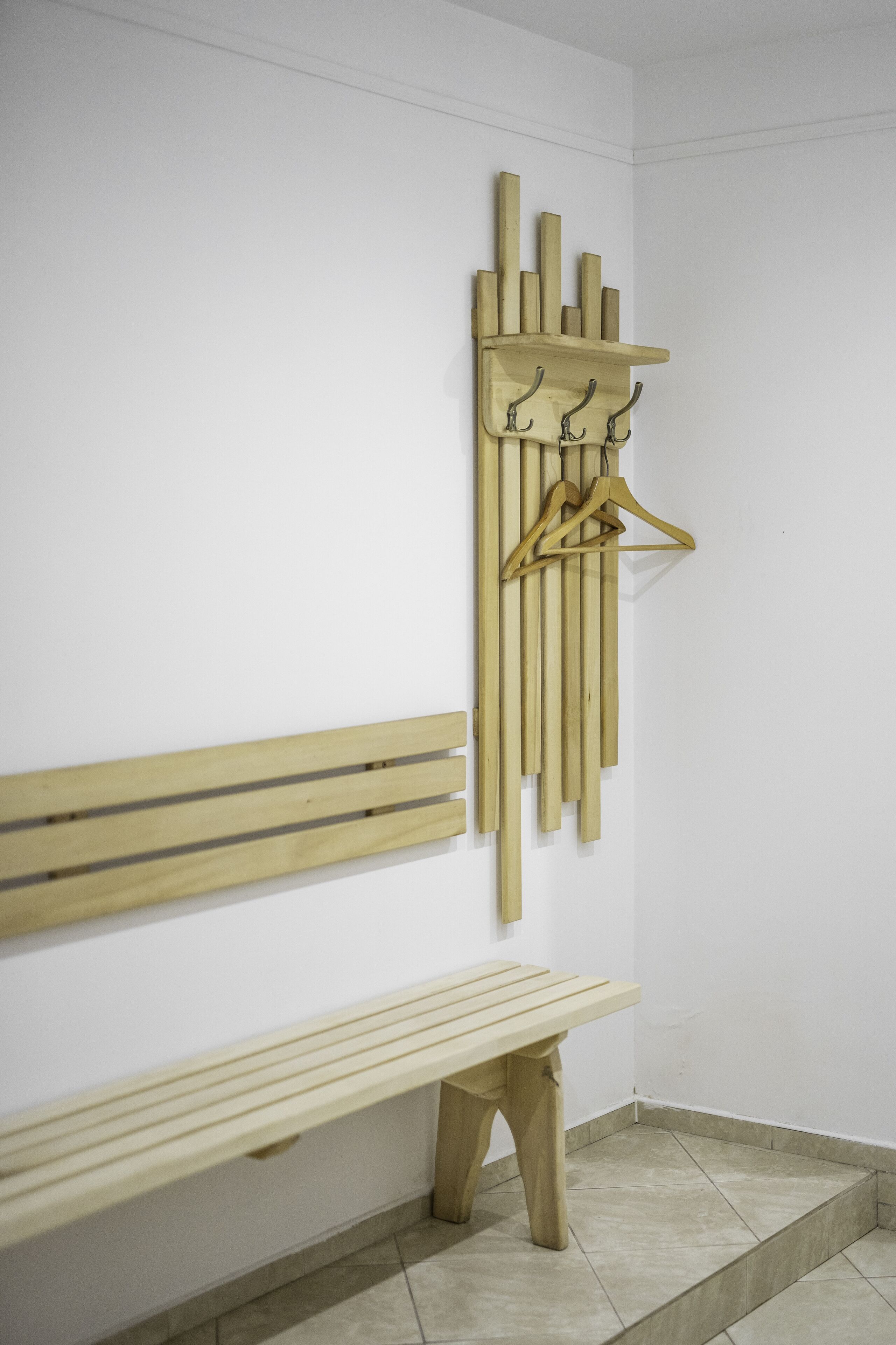 A wooden bench and a wall-mounted rack with hooks and a hanger.