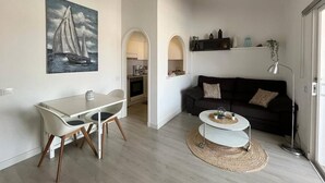 Un salon moderne comprenant un coin repas, un canapé noir, une table basse blanche et un tableau représentant un voilier.