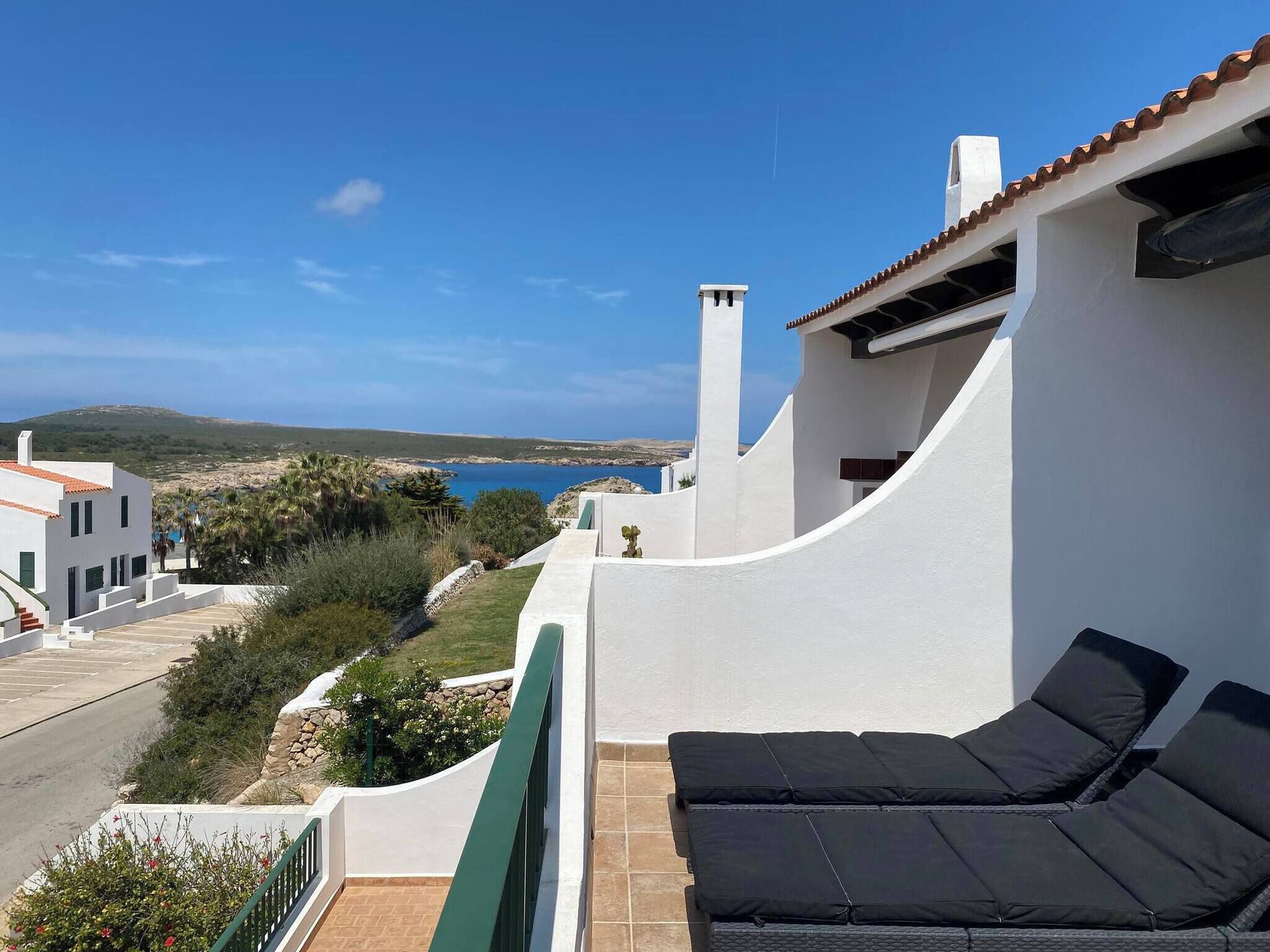 A balcony with a view of the sea, white walls, and a black outdoor sofa.