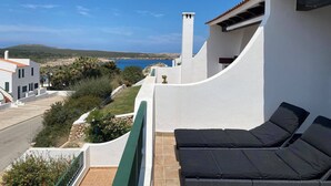 Un balcon avec vue sur la mer, des murs blancs et un canapé noir pour l’extérieur.