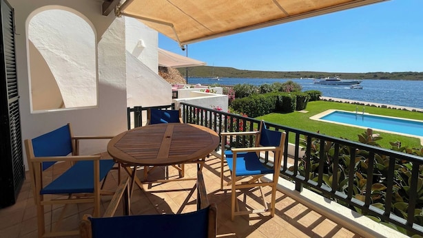 Un balcon avec une table et des chaises, donnant sur une piscine et offrant une vue panoramique sur la mer.